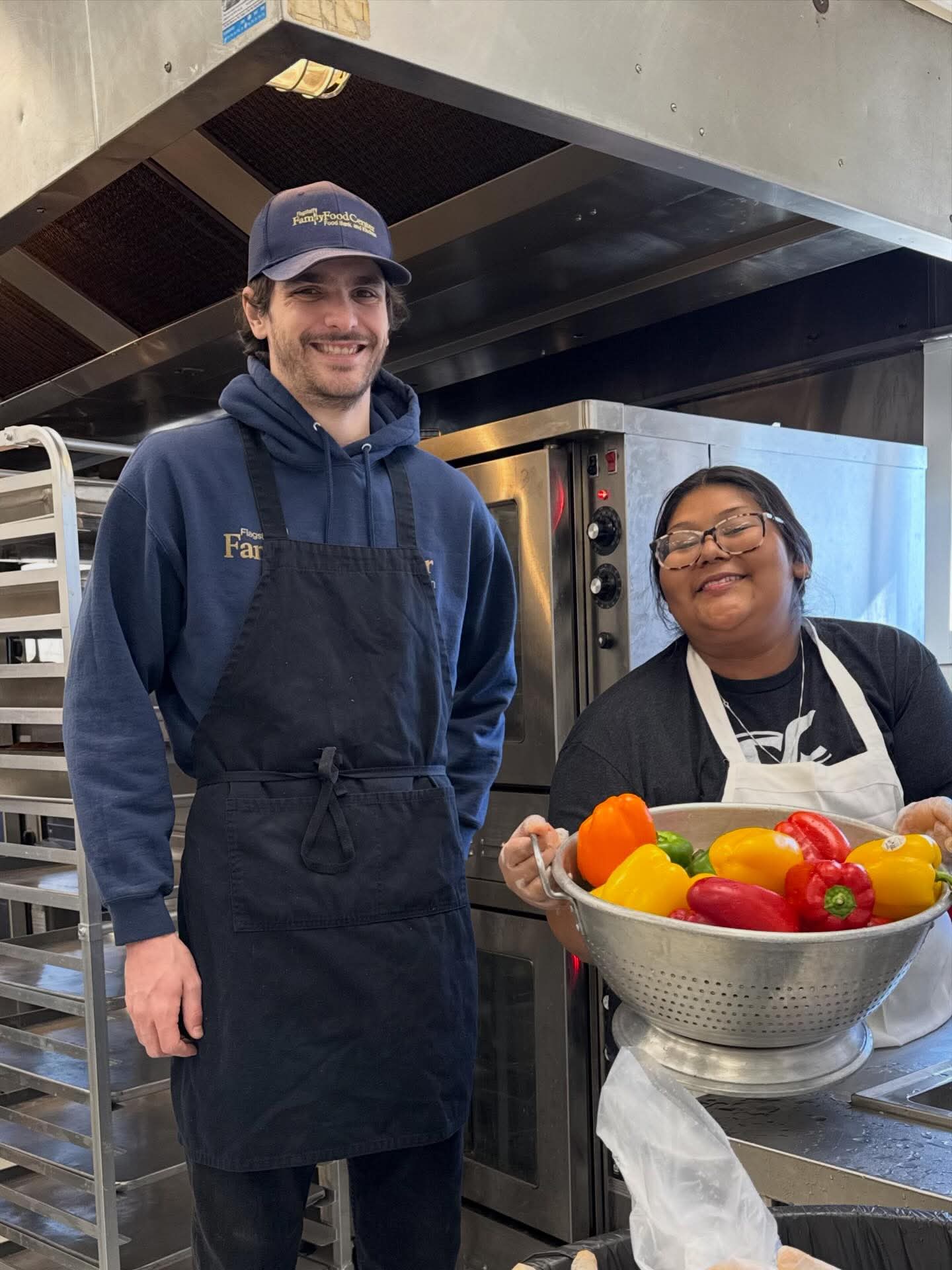 Two people in the Flagstaff Family Food Center kitchen, one holding a colander of colorful peppers